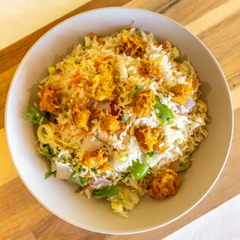 Close-up of a bowl of fried rice with chicken pakora, green peppers, and cilantro.