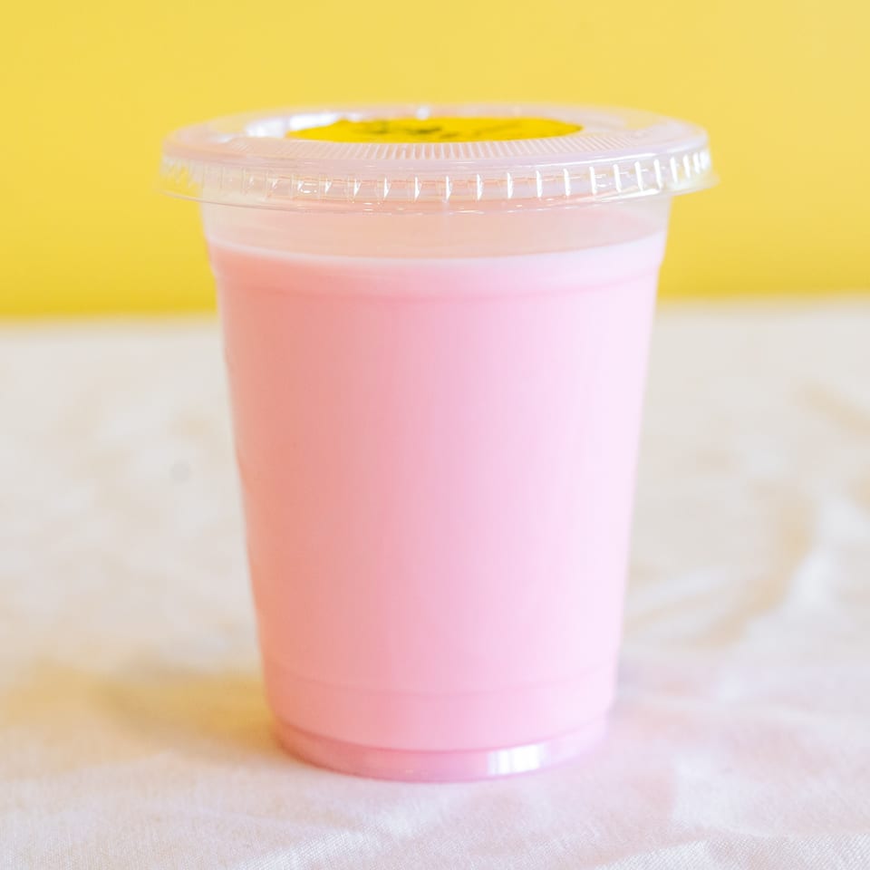 Pink beverage in a clear plastic cup with a lid and yellow sticker, against a yellow background.