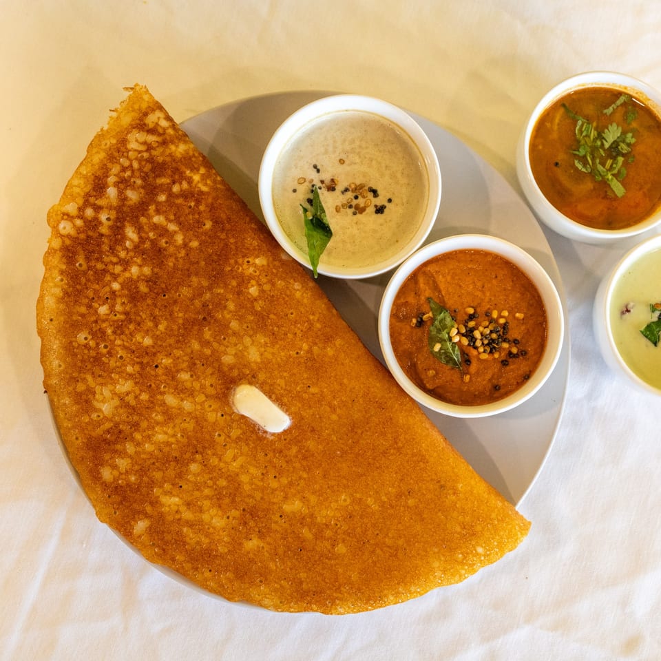Golden brown dosa with a dollop of butter, served with three bowls of colorful chutneys and sambar.