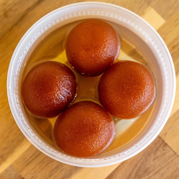 Four gulab jamun, Indian fried dough balls, soaking in syrup in a white plastic container.
